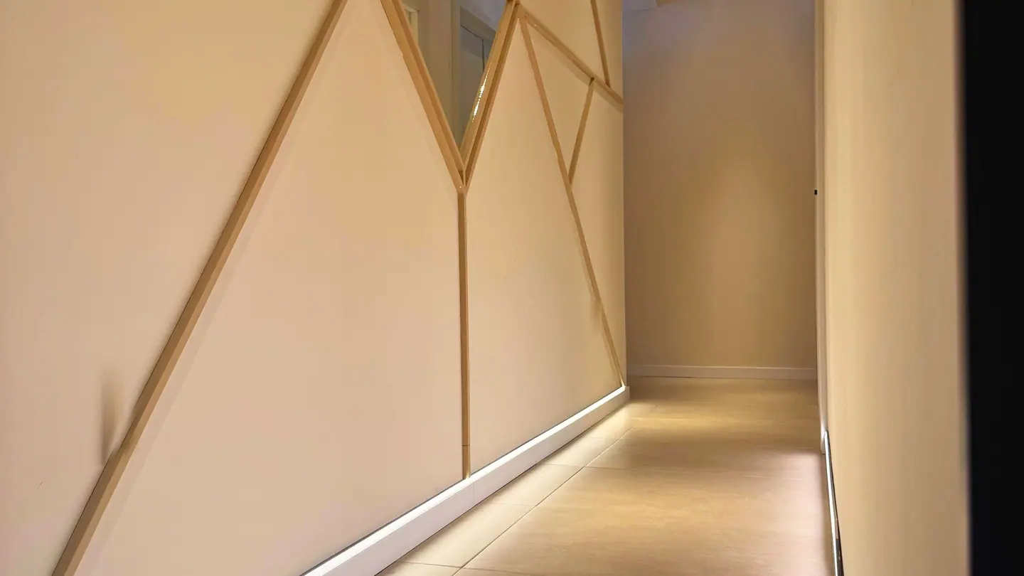 The corridor: brass battens set in a chevron across a cream wall, with concealed light running along the skirting.